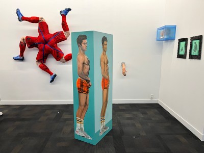 A gallery booth featuring a standing statue depicting Zac Efron (center), a statue of a football player's feet attached to the wall (left), and a limp wrist holding an iced coffee (right).
